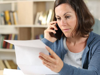 Serious adult woman checking letter calling on phone at home