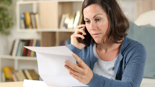 Serious adult woman checking letter calling on phone at home
