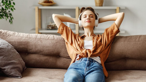Pleased young woman in headphones listening to music while relaxing on sofa at home