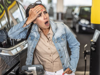 Woman refuelling the tank of her car with diesel looks shocked with mouth open seeing the high price of fuel.