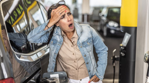 Woman refuelling the tank of her car with diesel looks shocked with mouth open seeing the high price of fuel.