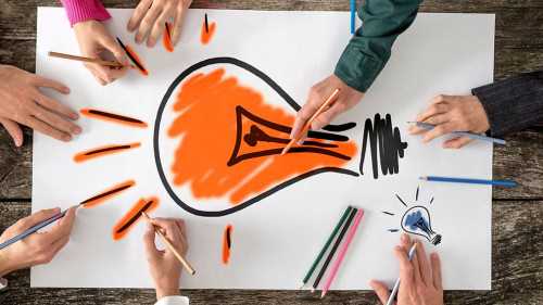 Six people, men and women, drawing bright yellow light bulb on a