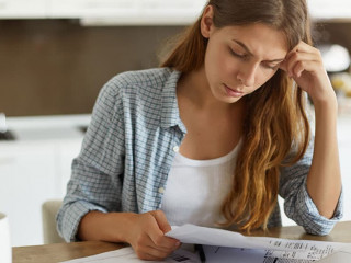 Indoor shot of casually dressed young woman holding papers in her hands, calculating family budget, trying to save some money to buy new bicycle to her son, having stressed and concentrated look