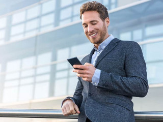Businessman using mobile phone app texting outside of office in urban city with skyscrapers buildings in the background. Young caucasian man holding smartphone for business work.