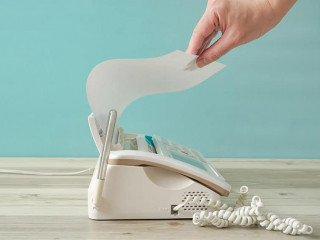 One person taking a paper from a fax machine. A person sending p