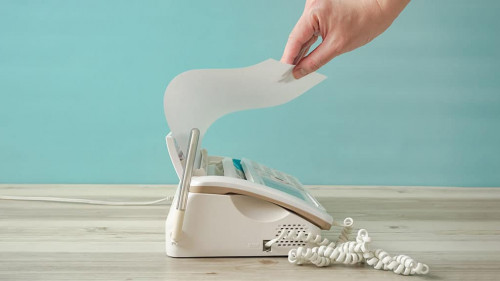 One person taking a paper from a fax machine. A person sending p