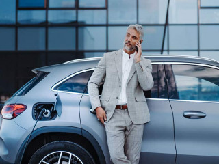 Businessman holding smartphone while charging car at electric vehicle charging station, closeup.
