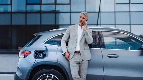 Businessman holding smartphone while charging car at electric vehicle charging station, closeup.