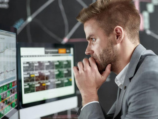 Keep growing with smart ideas. Portrait of successful young trader looking focused while sitting in front of multiple monitors in the office. Blackboard full of chart and data analyses in background.