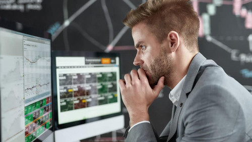Keep growing with smart ideas. Portrait of successful young trader looking focused while sitting in front of multiple monitors in the office. Blackboard full of chart and data analyses in background.