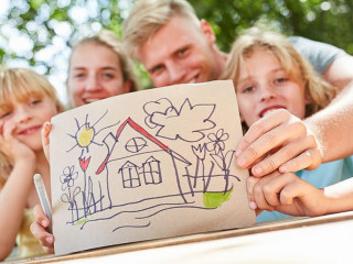 Familie zeigt bunte Zeichnung mit Eigenheim