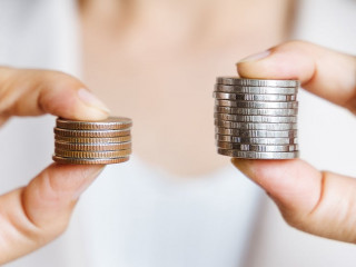 Hands compare two piles of coins of different sizes.