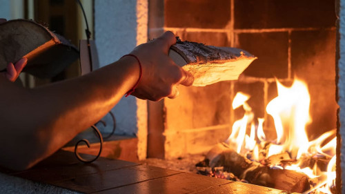 Hands put firewood in a kindled fireplace on a cold winter day.