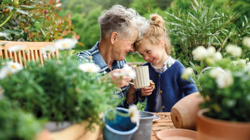 Senior grandmother with small granddaughter gardening on balcony in summer, resting.