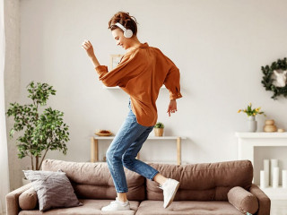 Cheerful woman listening to music and dancing on soft couch at home in day off