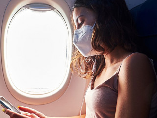 young girl wearing face mask using smartphone while traveling on