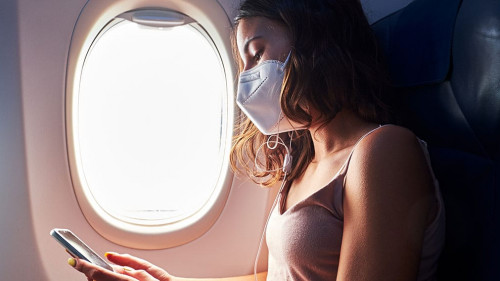 young girl wearing face mask using smartphone while traveling on