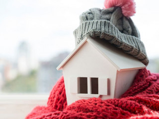 house in winter - heating system concept and cold snowy weather with model of a house wearing a knitted cap