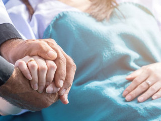 Male doctor holding female patient hand on the hospital bed.