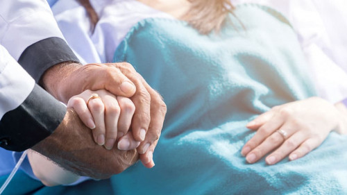 Male doctor holding female patient hand on the hospital bed.
