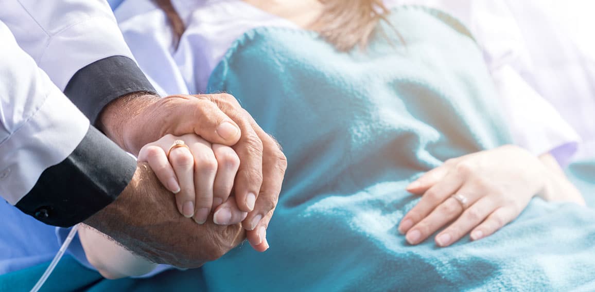 Male doctor holding female patient hand on the hospital bed.