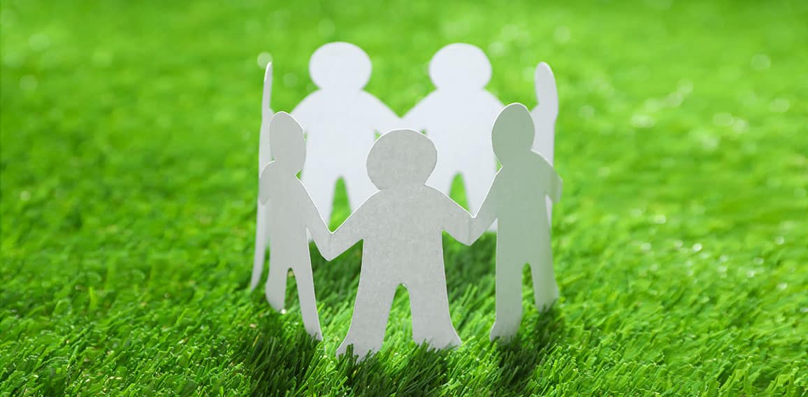 Paper people chain making circle on green grass. Unity concept