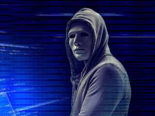 Hacker in mask with laptop on dark background