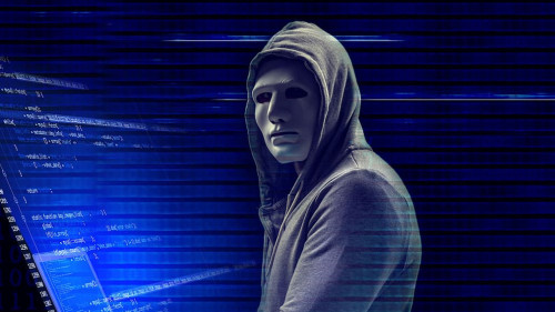 Hacker in mask with laptop on dark background