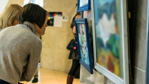 rear view of younga caucasian woman stading in an art gallery in front of two large colorful paintings