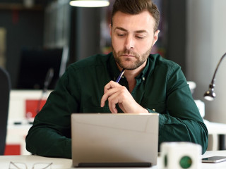 Young man studying with laptop computer on white desk.