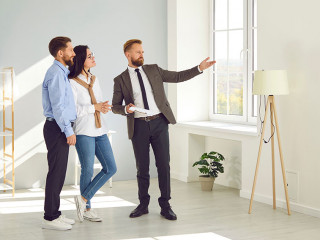 Real estate agent young man showing new big modern flat to couple of buyers or tenants.