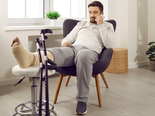 Young man is lying on the couch at home with broken leg in gypsum.