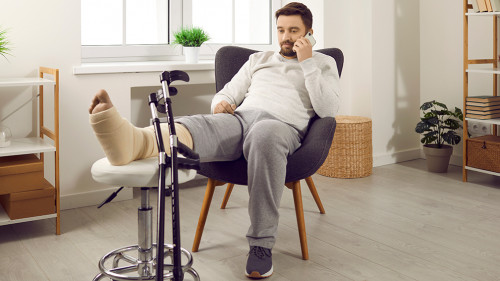 Young man is lying on the couch at home with broken leg in gypsum.