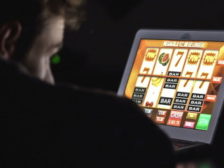 Gambling addicted man in front of online casino slot machine on laptop computer at night.