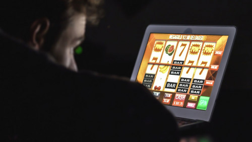 Gambling addicted man in front of online casino slot machine on laptop computer at night.