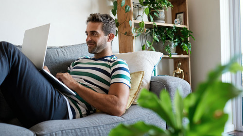 Smiling young man using a laptop on his sofa