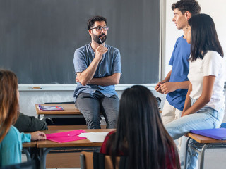 Group of teenagers with young male teacher at classroom, sitting talking and discussing together