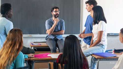 Group of teenagers with young male teacher at classroom, sitting talking and discussing together