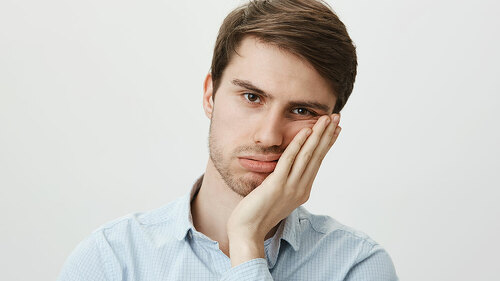 Indoor shot of upset irritated caucasian guy leaning on palm and sighing at camera, being bored and fed up of annoying meeting in office, wanting to go home, tired of wasting time over gray wall