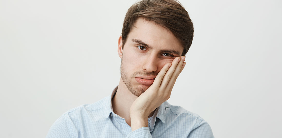 Indoor shot of upset irritated caucasian guy leaning on palm and sighing at camera, being bored and fed up of annoying meeting in office, wanting to go home, tired of wasting time over gray wall