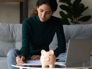 Satisfied woman checking finances, sitting at table with piggy bank
