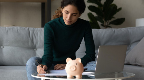 Satisfied woman checking finances, sitting at table with piggy bank