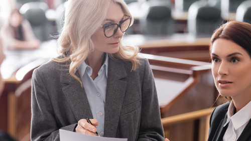prosecutor pointing with hand while talking to blurred judge near attorney in courtroom