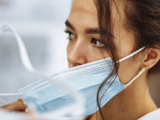 Tired nurse takes off a protective face shield and medical mask after a tough working shift at the hospital. Female doctor fights the coronavirus pandemic working hard overtime and being exhausted.