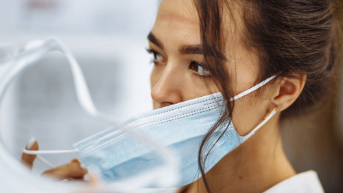 Tired nurse takes off a protective face shield and medical mask after a tough working shift at the hospital. Female doctor fights the coronavirus pandemic working hard overtime and being exhausted.