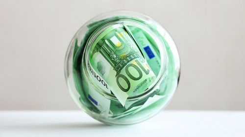 Euro banknotes in a glass jar on a grey background