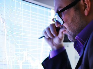 A businessman is looking at a graph on a monitor. An exchange br