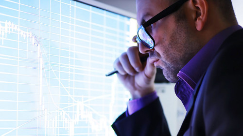 A businessman is looking at a graph on a monitor. An exchange br