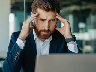 Depressed middle aged businessman looking at laptop and touching head, suffering from headache or having problems