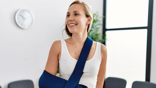 Young caucasian woman wearing sling on arm for accident standing at clinic waiting room